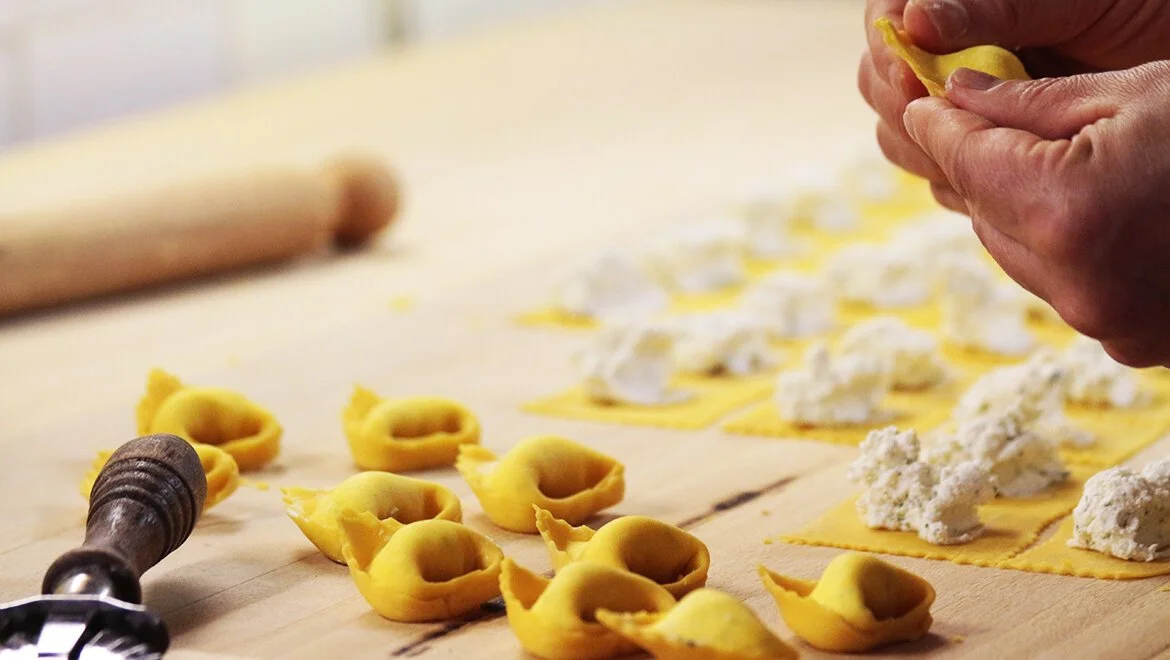 Handmade tortellini pasta preparation: Close-up of hands shaping pasta, alongside fresh, uncooked tortellini.